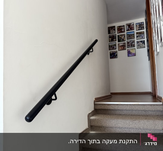 מאחז יד שחור ממתכת המותקן על קיר לצד מדרגות פנימיות